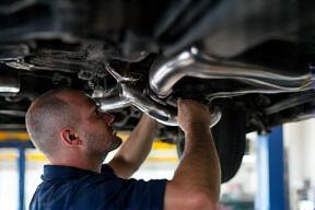 Mechanic checking exhaust pipe under car